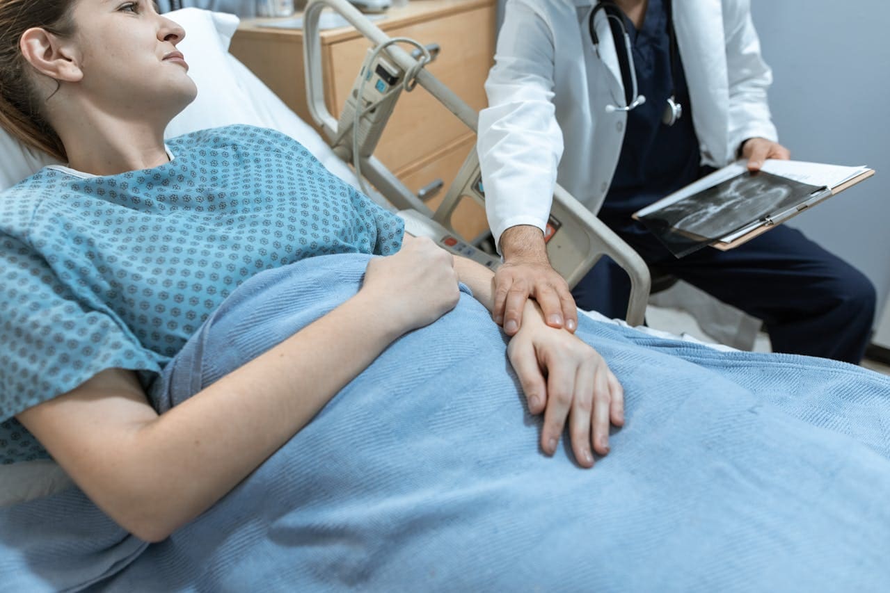 A doctor touches the arm of a female patient as she lays in a hospital bed.