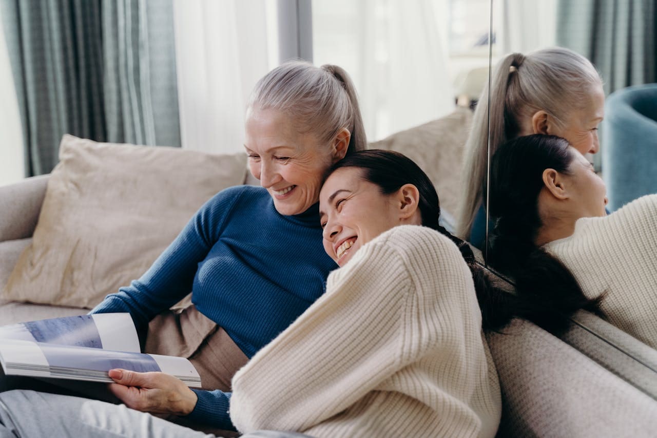An older woman with her adult daughter sitting on the couch looking at a photo album.