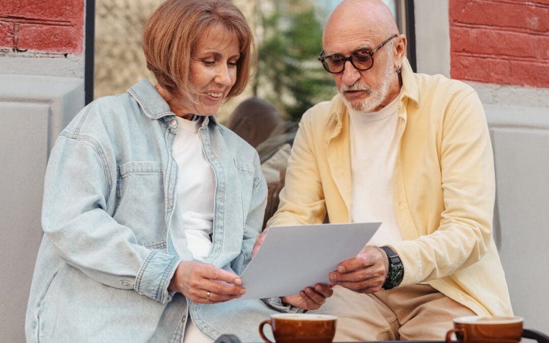 An older, white couple talks over some papers at a coffee shop.