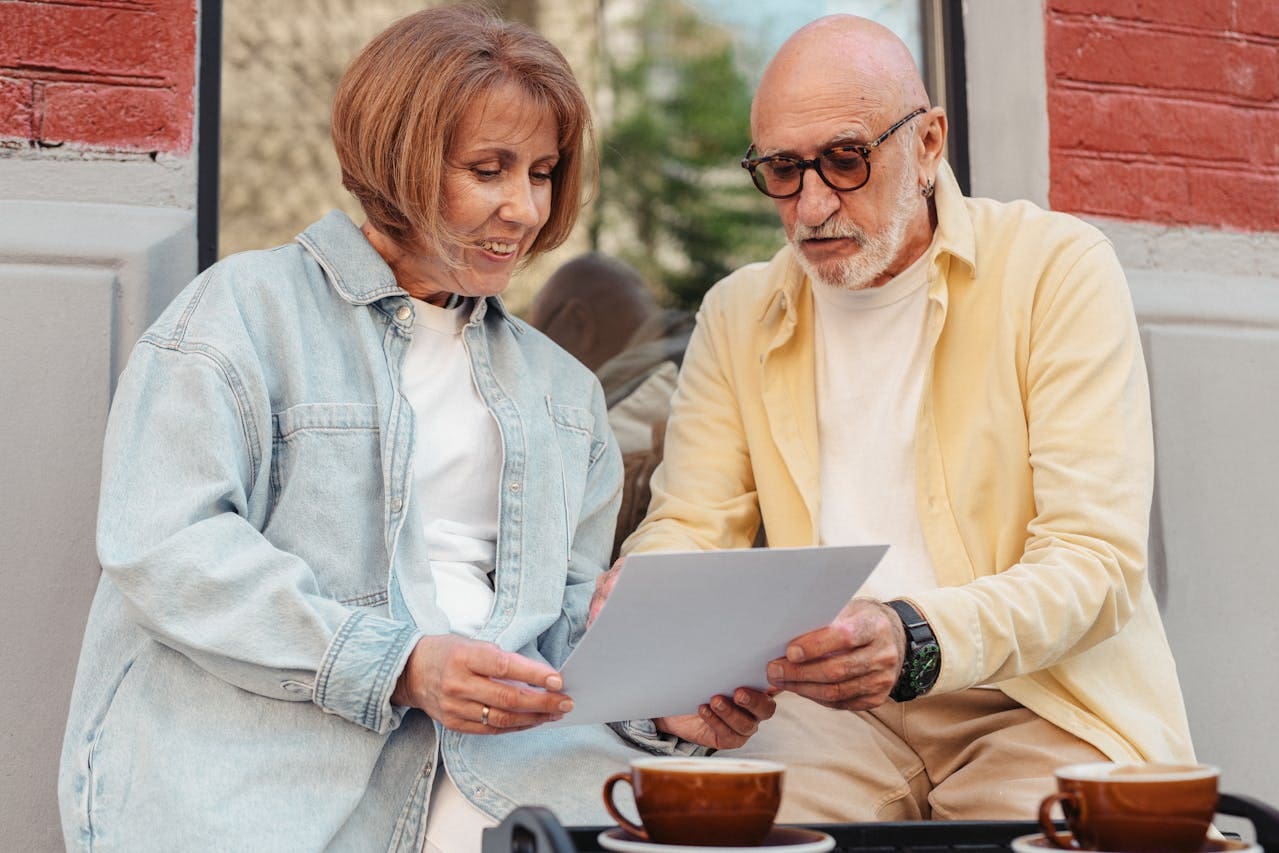 An older, white couple talks over some papers at a coffee shop.